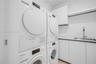 Laundry room featuring stacked front-load appliances, built-in cabinetry with solid-surface countertops, an undermount sink, and wall-mounted shelving