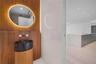 Wood-paneled wall feature with integrated backlit oval mirror, dark speckled pedestal basin, wall-mounted faucet, and stone-surfaced kitchen island wi