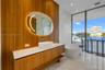 Floating wood-finish vanity with an integrated countertop, oval back-lit mirror, vessel sink, freestanding soaking tub, and floor-to-ceiling glass pan