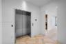 Stainless steel elevator with brushed metal finish, herringbone wood-finish flooring, and recessed ceiling lighting