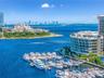 Aerial perspective of a deep-water marina featuring boat slips and a curved modern mid-rise building with floor-to-ceiling glass paneling and balcony 