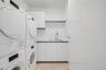 Utility area featuring stacked laundry appliances, white built-in cabinetry, a rectangular stainless steel sink with a high-arch pull-down faucet, and