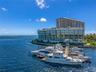 Waterfront multi-story residential building featuring floor-to-ceiling glass paneling, wraparound balconies, and a private deep-water marina