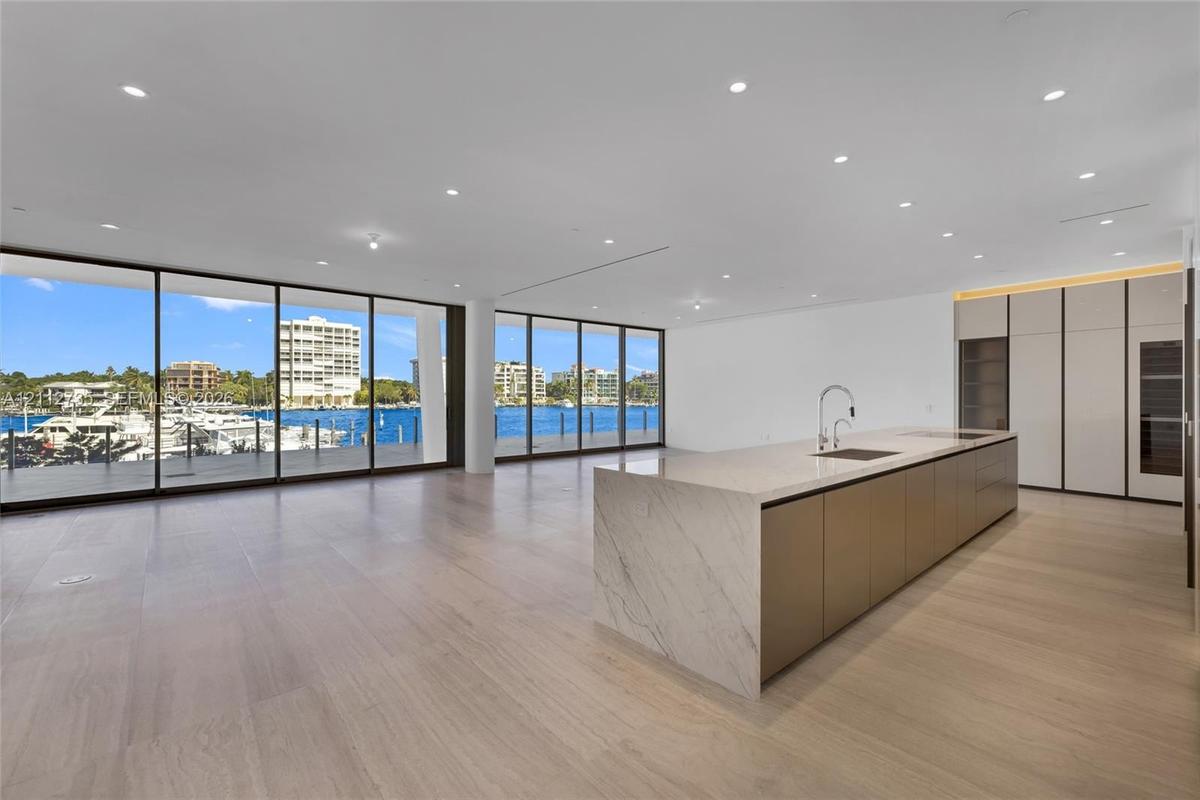 Open-concept interior featuring floor-to-ceiling glass walls, expansive kitchen island with a stone-finish waterfall countertop, built-in floor-to-cei