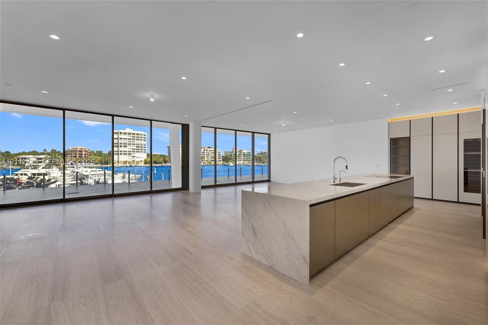 Open-concept interior featuring floor-to-ceiling glass walls, expansive kitchen island with a stone-finish waterfall countertop, built-in floor-to-cei