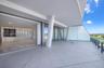 Expansive covered terrace featuring large-format tile flooring, structural pillars, and glass railings, with interior space showcasing wood-finish flo