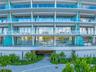 Contemporary multi-story facade featuring floor-to-ceiling glass windows, wraparound balconies with glass railings, structural white pillars, and land