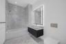 Full-height stone wall tiling, floating vanity with vessel sink, wall-mounted faucet, illuminated mirror, and wall-mounted dual-flush toilet