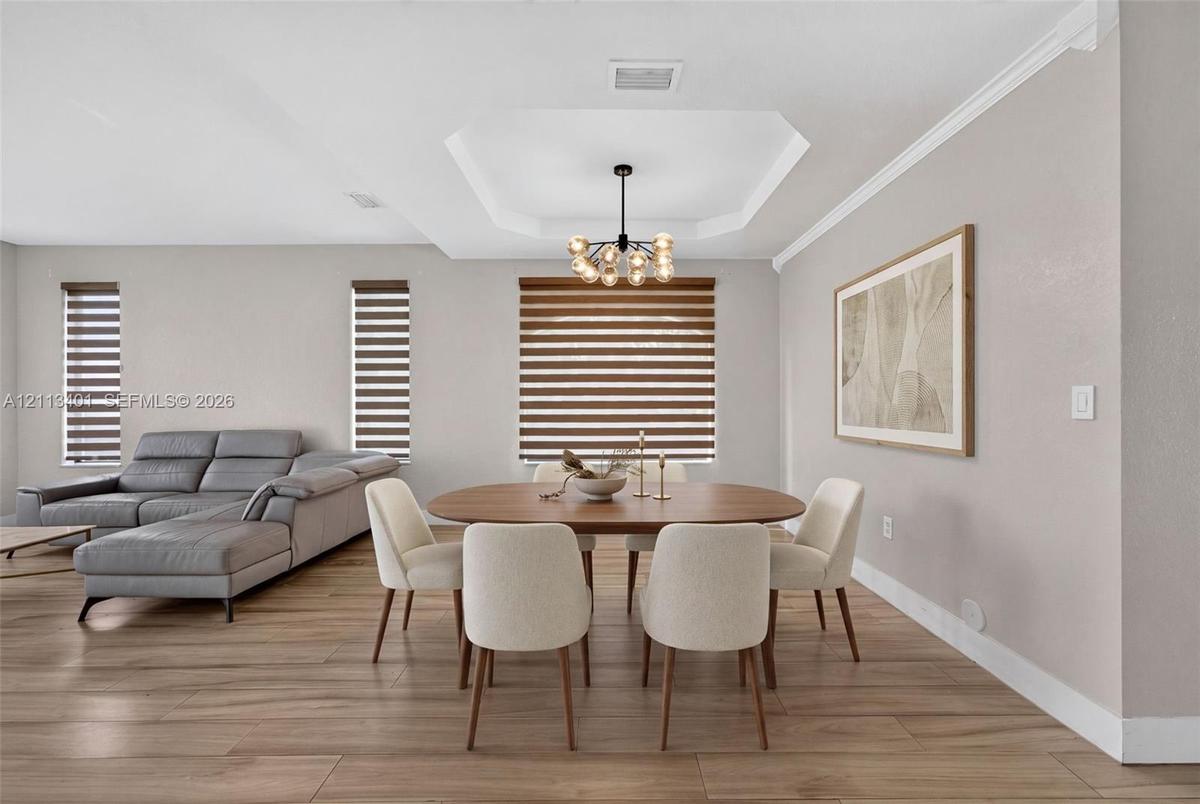 Tray ceiling, wood-finish flooring, multi-light orb chandelier, and dual-shade window treatments