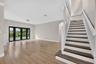Open-concept interior featuring wood-finish flooring, a staircase with white balusters and dark wood-finish treads, crown molding, and black-framed gl