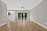 Open-concept area featuring wood-finish flooring, white cabinetry, a stone-finish waterfall-edge peninsula, and black-framed glass french doors