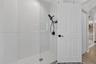 Walk-in shower with white subway tile surround, glass partition, matte black handheld shower fixture, and wood-finish flooring