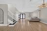 Wood-finish flooring, white staircase with dark treads, tray ceiling, multi-bulb chandelier, and glass-paneled double entry doors