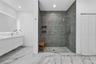 Floating dual-sink vanity with under-cabinet lighting, walk-in shower with frameless glass enclosure, floor-to-ceiling stone-look wall tile, pebble-te