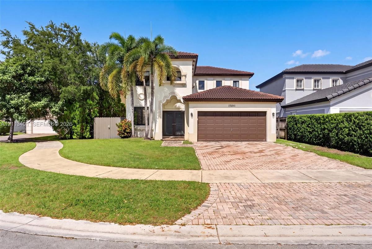Two-story stucco exterior featuring a tiled roof, arched entryway, brick-paver driveway, and an attached two-car garage