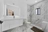 Floating white vanity with integrated sink, expansive LED-backlit mirror, floor-to-ceiling stone-look wall tiles, walk-in glass-enclosed shower, and m