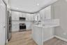 Kitchen featuring white shaker-style cabinetry, a stone-patterned waterfall countertop, stainless steel appliances, and wood-finish flooring
