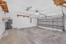 Two-car garage featuring a concrete floor, built-in wooden wall shelving, overhead fluorescent lighting, an automated door opener, and a dedicated wat