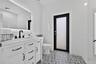 White vanity with a light-toned countertop, matte black hardware, integrated backsplash, backlit mirror, and patterned tile flooring