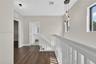 Hallway featuring wood-finish flooring, white railing with vertical balusters, trio pendant lighting, and neutral wall tones