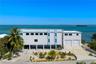 Multi-level coastal residence featuring an elevated structure, rooftop terrace with railing, dual garage bays, expansive concrete driveway, and direct