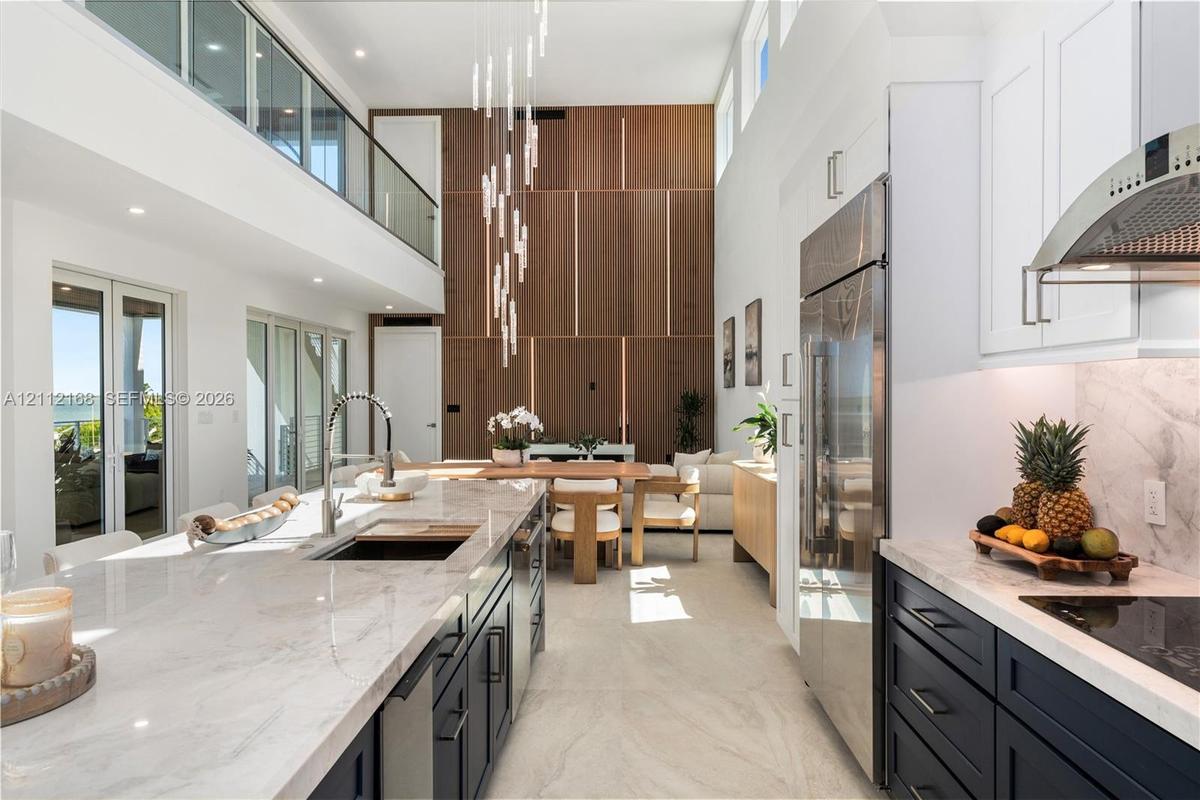 Double-height ceilings, floor-to-ceiling wood-panel accent wall, dual-tone cabinetry with stone-finish countertops, stainless steel integrated applian
