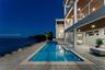 Multi-level structure featuring expansive covered balconies with horizontal cable railings, tile-surround swimming pool, integrated spa, and expansive