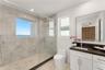 Bathroom featuring a walk-in shower with large-format wall tile and pebble-texture flooring, frameless glass enclosure, dual-pane window, and white ca