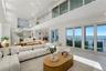 Expansive open-concept living area featuring double-height ceilings, a floor-to-ceiling glass-paneled mezzanine, multi-panel sliding glass doors, and 