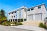 Multi-story contemporary exterior featuring a concrete facade, dual roll-up garage doors, a concrete vehicle ramp, and exterior wall-mounted lighting