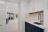 Wet bar featuring dark blue cabinetry, stone-finish countertop, coordinating backsplash, undermount stainless steel sink, and a gooseneck faucet