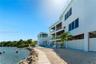 Multi-level waterfront exterior featuring white stucco siding, glass-panel railings, covered balconies, an inground swimming pool, and stone-lined sho
