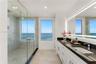 Dual-vanity bathroom featuring white cabinetry, dark stone countertops, a large frameless glass-enclosed shower with stone tile flooring, and a full-l