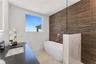 Freestanding soaking tub featuring a wall-mounted faucet, horizontal slatted wood-texture accent wall, glass partition, stone-finish vanity countertop
