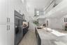 High-ceilinged kitchen featuring dual-tone cabinetry, a waterfall-edge stone island, recessed lighting, and a glass-panel staircase railing