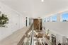 Elevated walkway featuring a sleek glass railing, wood-finish flooring, soaring ceilings, clerestory windows, and a multi-tiered modern chandelier