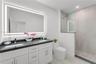 Double vanity with dark countertops, integrated rectangular sinks, wall-to-wall LED backlit mirror, walk-in glass shower with stone-style tile surroun