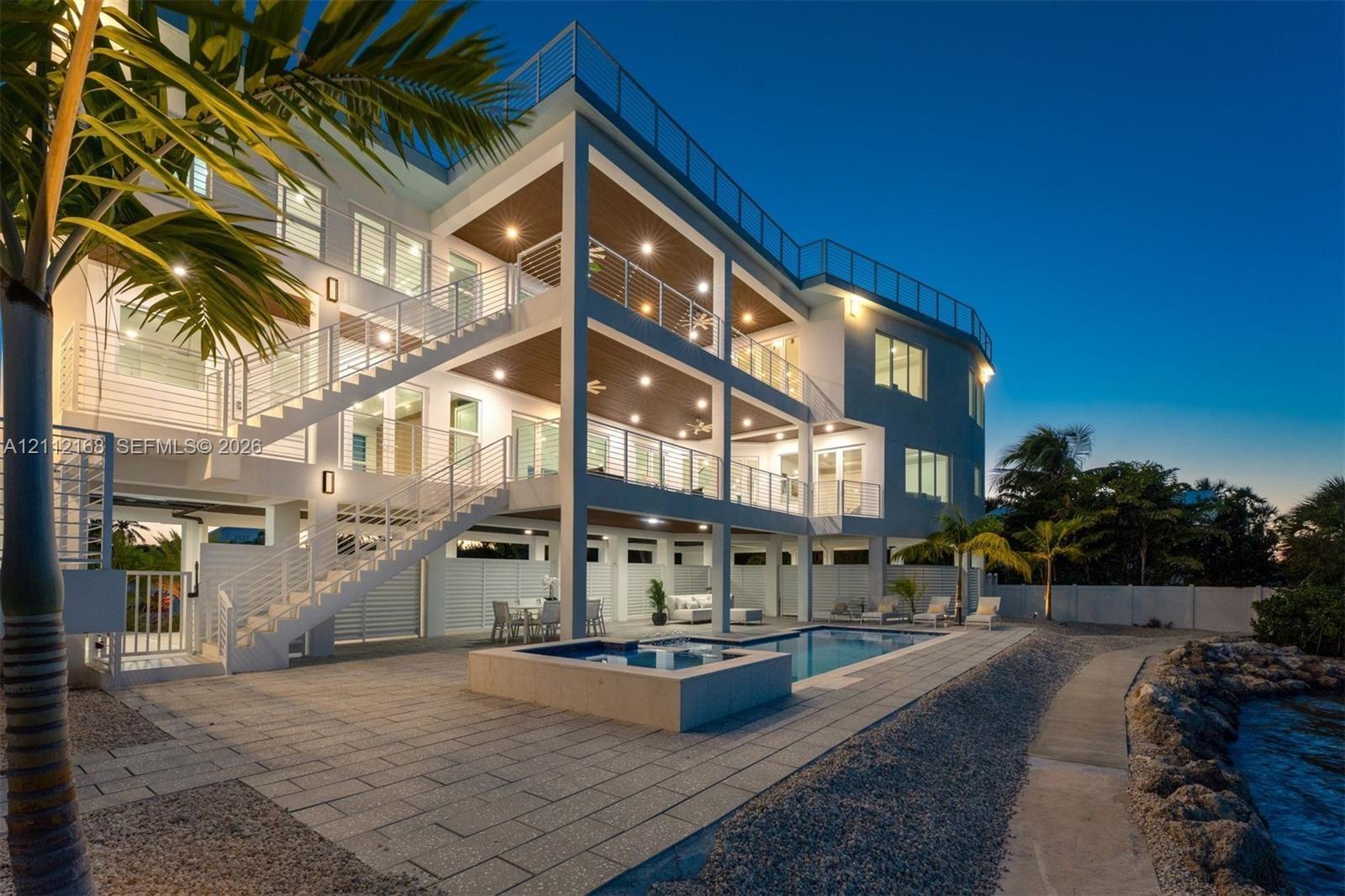 Multi-level exterior featuring stacked covered balconies, a rooftop terrace with horizontal cable railings, a built-in swimming pool and spa, and ston