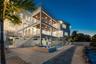 Multi-level exterior featuring stacked covered balconies, a rooftop terrace with horizontal cable railings, a built-in swimming pool and spa, and ston