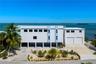 Multi-level contemporary exterior featuring a concrete facade, two-car garage, covered ground-level parking, rooftop railing, and waterfront orientati