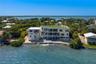 Waterfront multi-story residence featuring a ground-level swimming pool, expansive elevated balconies, stone-reinforced shoreline, and a rooftop deck