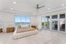 Tray ceiling with recessed lighting, ceiling fan, large windows, and floor-to-ceiling glass panel doors opening to a covered terrace