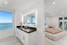 Bathroom vanity featuring white cabinetry, a dark countertop, integrated dual sinks, and an illuminated rectangular mirror, complemented by water-fron
