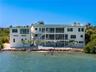 Multi-level waterfront structure featuring a white stucco exterior, tiered balconies with metal railings, an integrated ground-level swimming pool, an