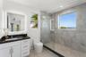 Bathroom featuring a white vanity with a dark countertop, an illuminated mirror, a glass-enclosed shower with large-format tile surround, and an integ