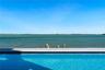 Infinity-edge pool with blue tiled waterline, stone paver decking, and open water frontage