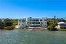 Waterfront multi-story residence featuring tiered exterior balconies, a ground-level swimming pool, and stone-reinforced shoreline