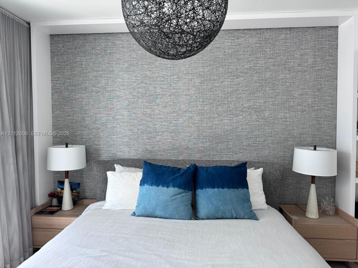 Textured gray wall accent, recessed built-in wood-finish nightstands, and spherical overhead pendant light fixture