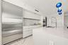 Modern kitchen featuring high-gloss cabinetry, a quartz waterfall island, stone-finish flooring, integrated stainless steel refrigeration, and a comme