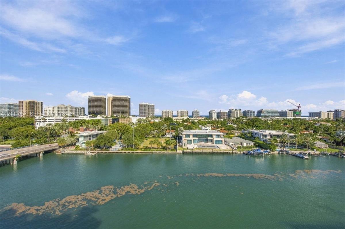 Waterfront estate featuring a paved pool deck, private dock, two-story structure with extensive glass glazing, and mature perimeter landscaping